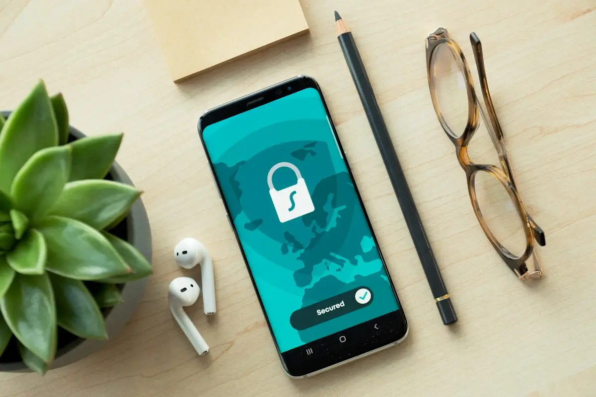 A phone showing a padlock screen on a desk with a pencil and glasses