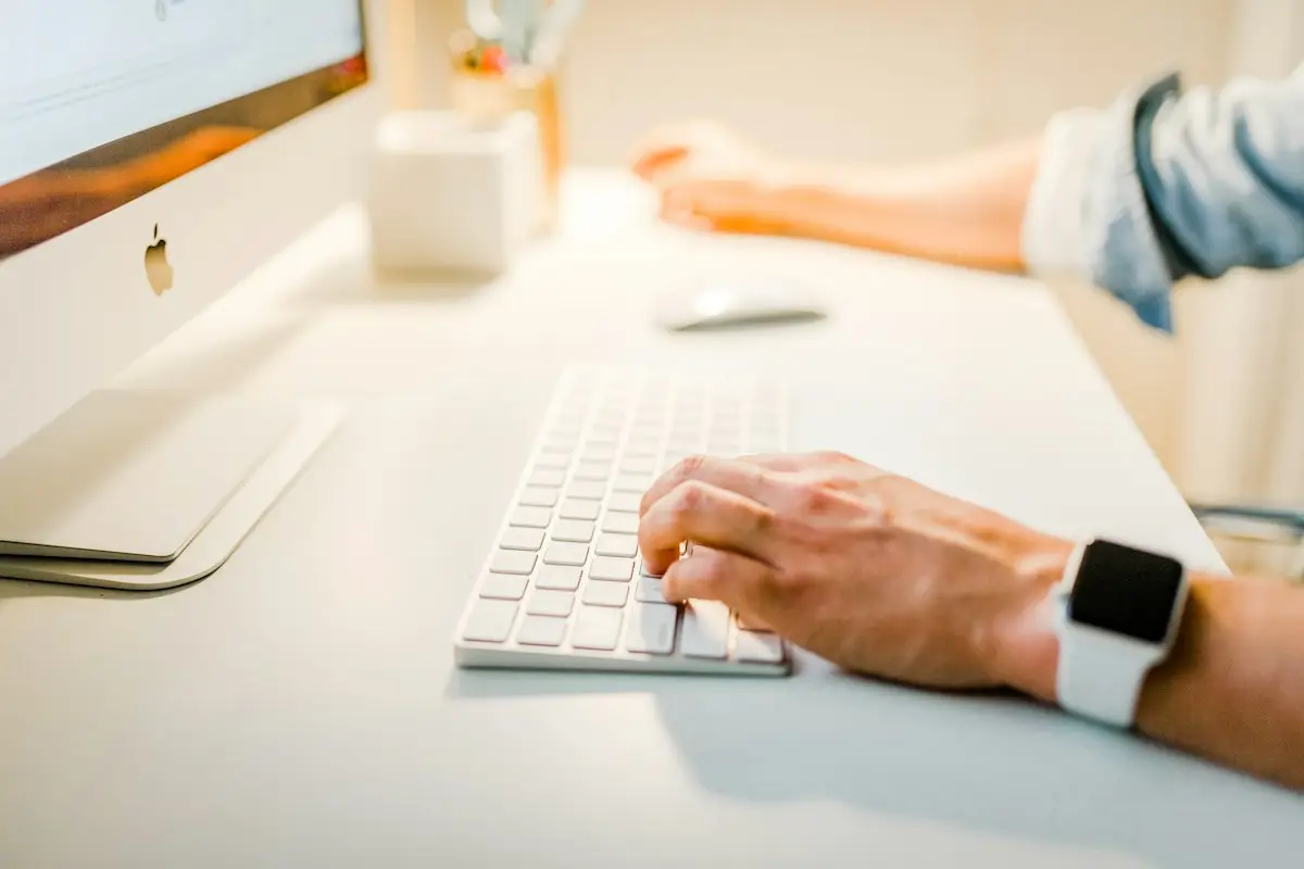 A hand on a white keyboard beside a monitor