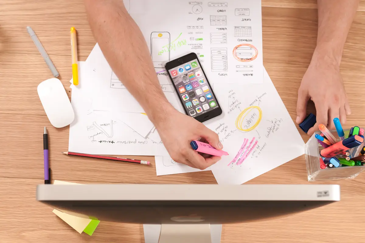 A desk with website wireframes, a phone and coloured pens