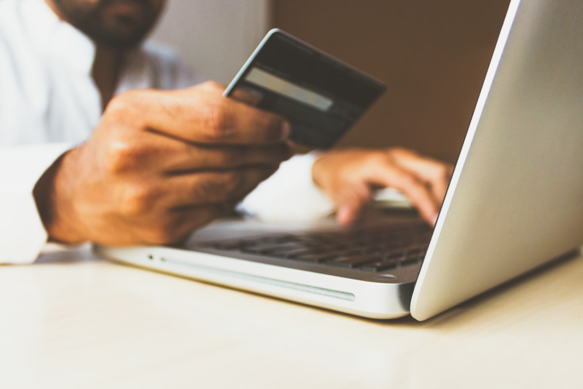 Person holding a bank card in one hand while typing on a laptop keyboard