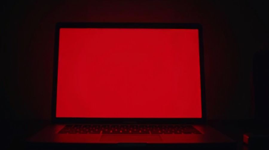 A laptop screen glowing flat red in a dark room, nobody at the desk