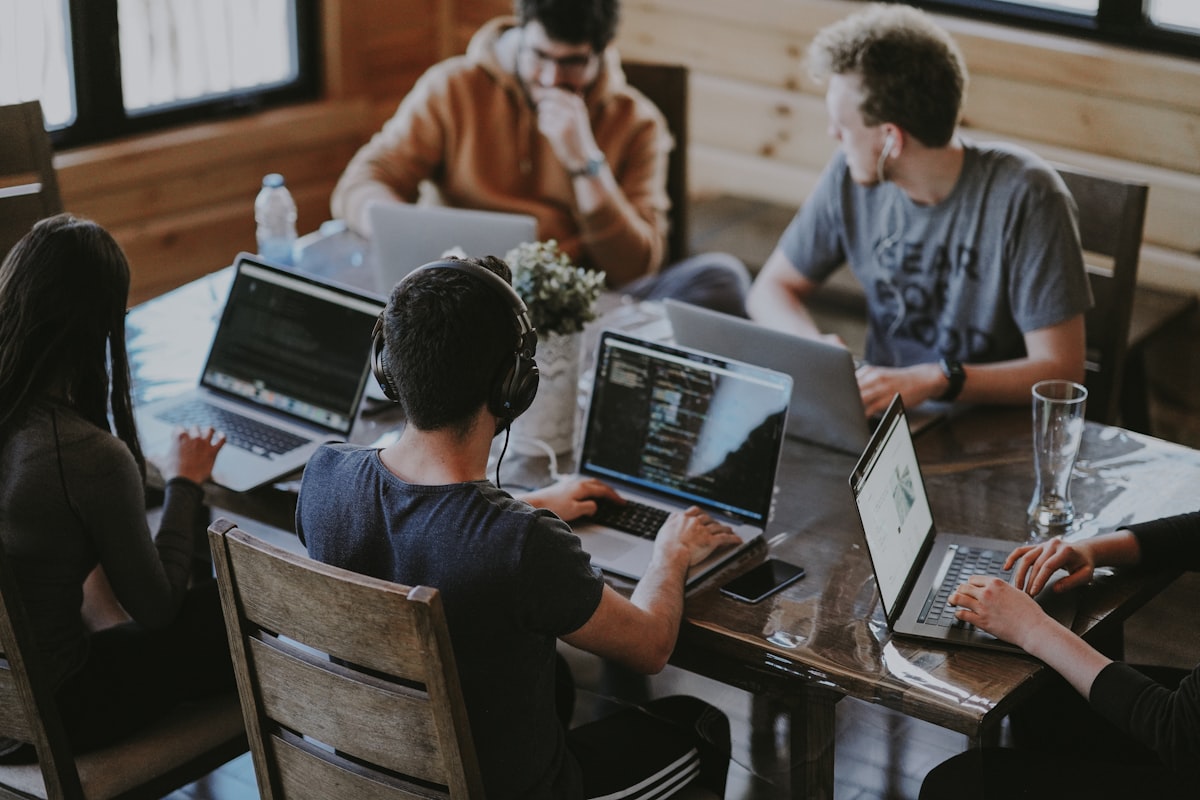 Four people working together at one table, laptops open with code on the screens