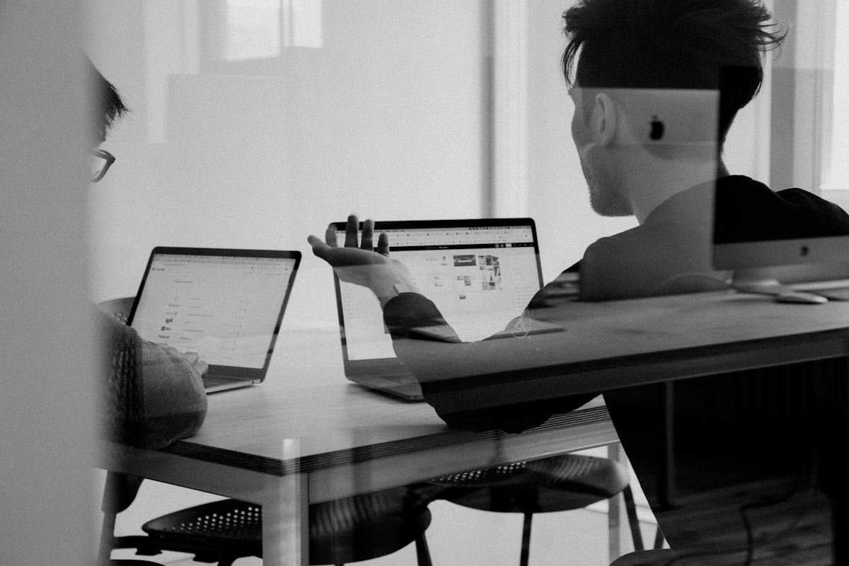 Two people discussing a project across their laptops at a meeting table