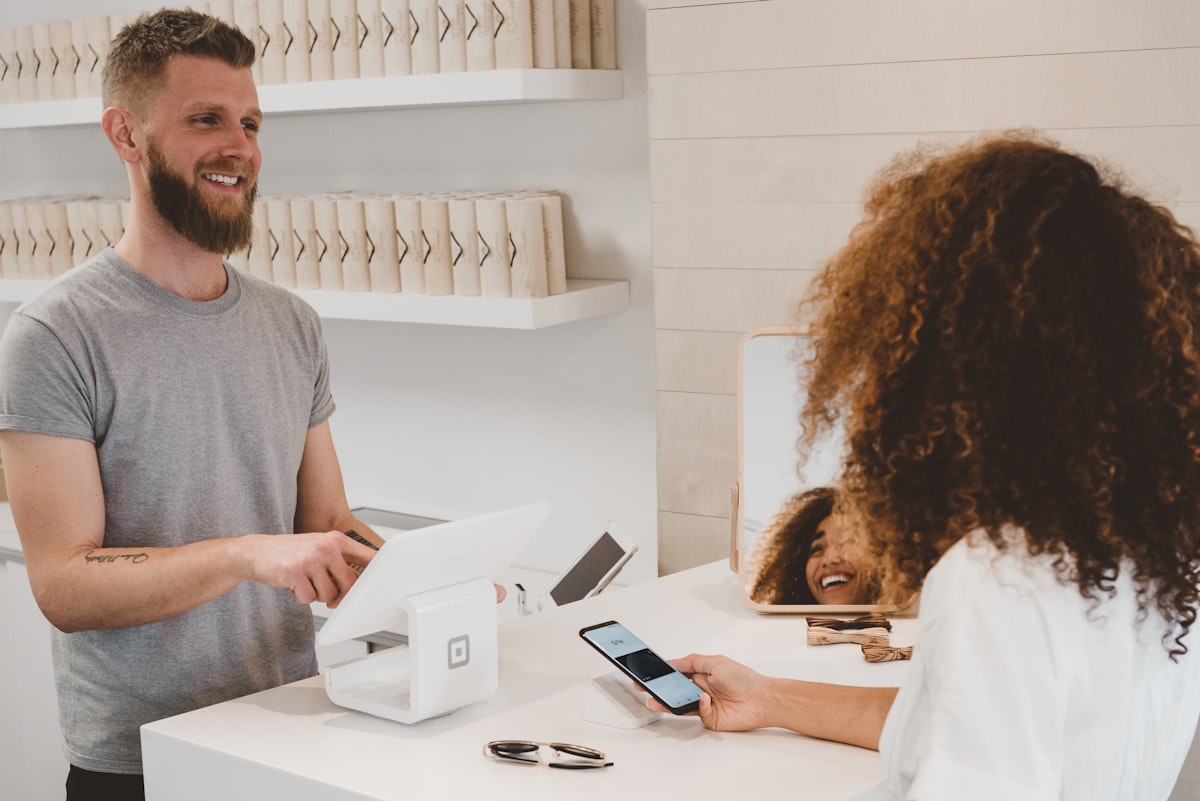 Shop assistant at a white payment terminal while a customer pays using her phone