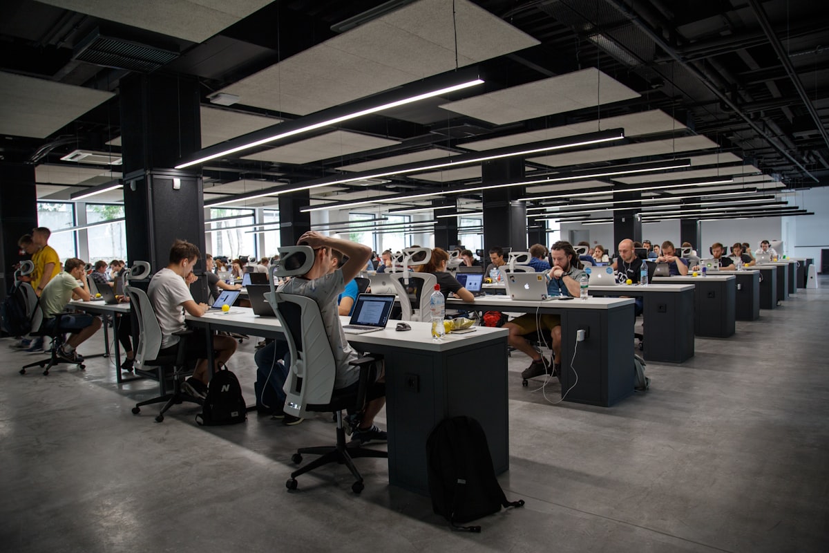 Large open-plan office with rows of desks where many people work at laptops under strip lighting