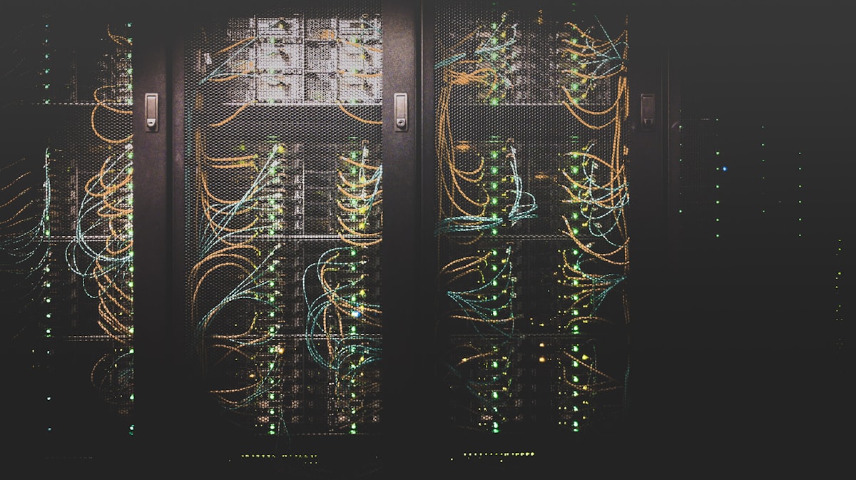 Dark data-centre server racks with orange and blue network cables and rows of green status lights