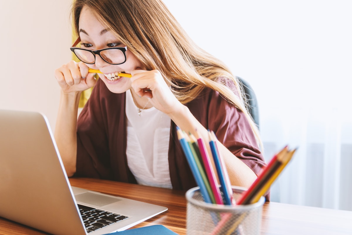 Person in glasses biting a pencil in frustration while staring at a laptop screen at a desk
