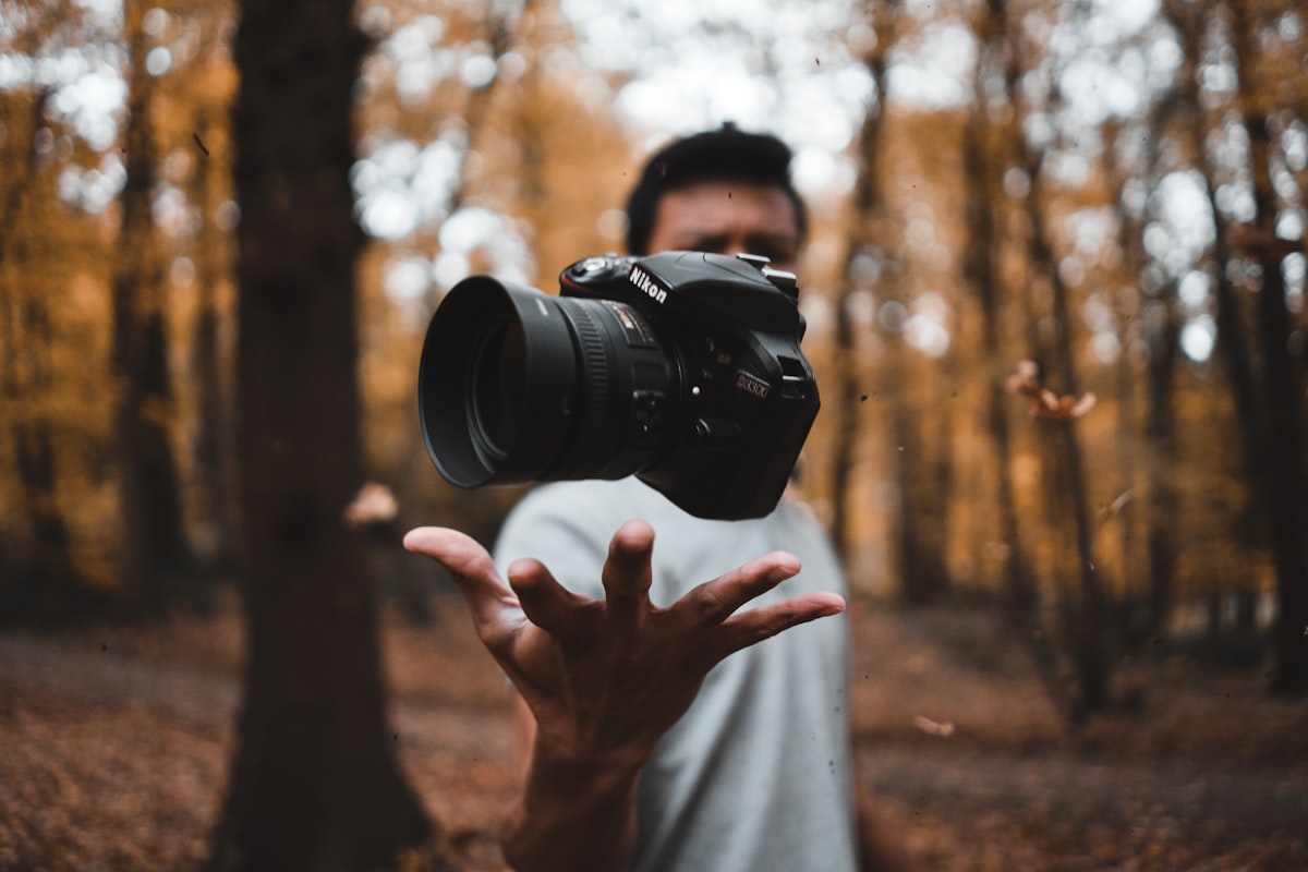 A person tossing a DSLR camera into the air in an autumn forest