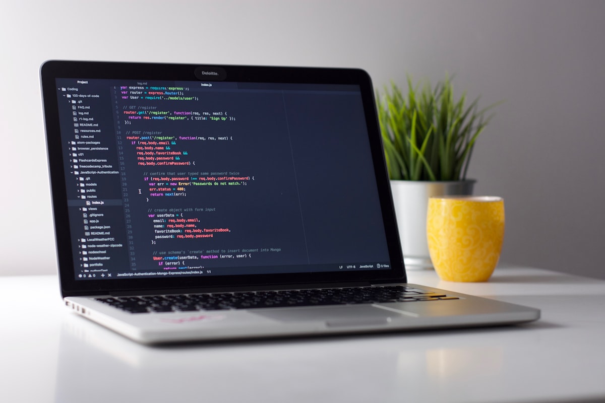 Laptop showing a code editor, with a plant and a yellow mug beside it